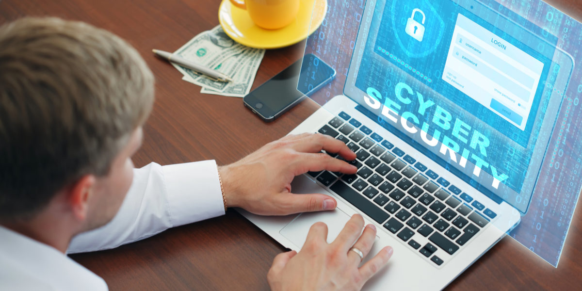 Man working on computer with cyber security image and dollar bills under his coffee mug